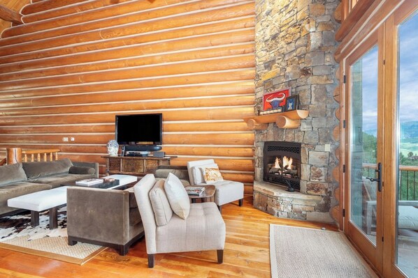 A log cabin interior with a stone fireplace, a television, and a sofa.