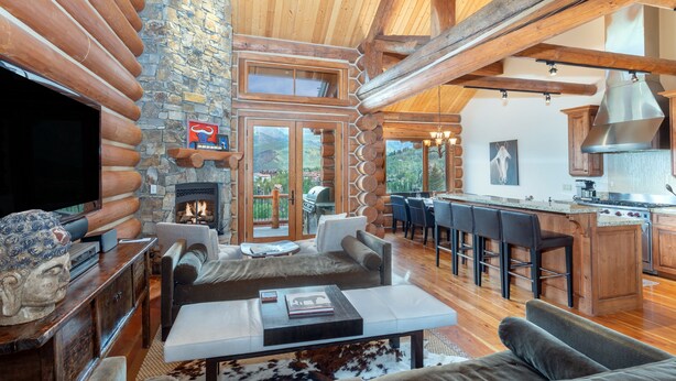A log cabin interior with a stone fireplace, wooden beams, a bar area, and a large TV. - Beautiful Ski-In/Ski-Out Log Townhome with Exceptional Views (Mountain Village)