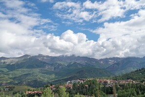 A mountain village with buildings nestled among green hills and a clear sky. - Townhomes on the Creek 117 (Mountain Village)