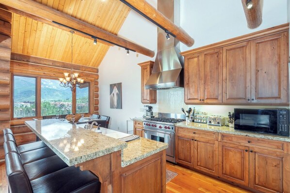 A kitchen with wooden cabinets, granite countertops, a large island, and a view of the outdoors. - Townhomes on the Creek 117 (Mountain Village)