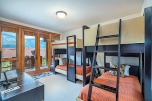 Une chambre avec des lits superposés, un bureau, une vue sur l’extérieur et une porte donnant sur un espace extérieur.