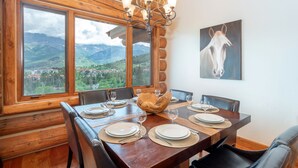 A dining area with a wooden table set for six, large windows, and a mountain view. - Beautiful Ski-In/Ski-Out Log Townhome with Exceptional Views (Mountain Village)