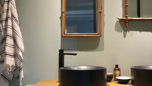 Un baño con tocador de madera, dos lavamanos negros, un espejo y una toalla colgada de un gancho.