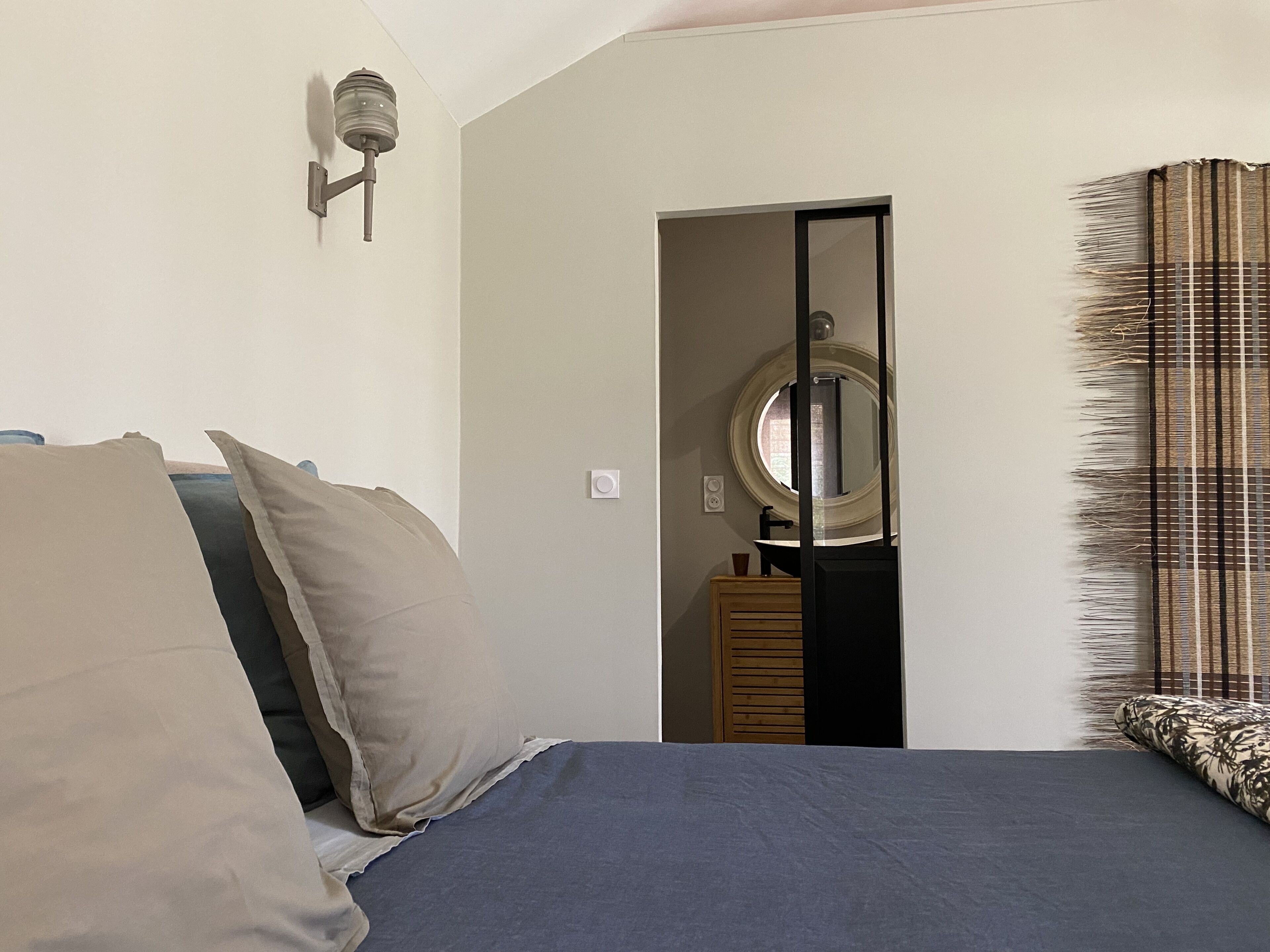 Ein Schlafzimmer mit Bett, Kissen, einem Nachttisch, einem Spiegel und einem Fenster mit Jalousien.
