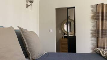 Ein Schlafzimmer mit Bett, Kissen, einem Nachttisch, einem Spiegel und einem Fenster mit Jalousien.