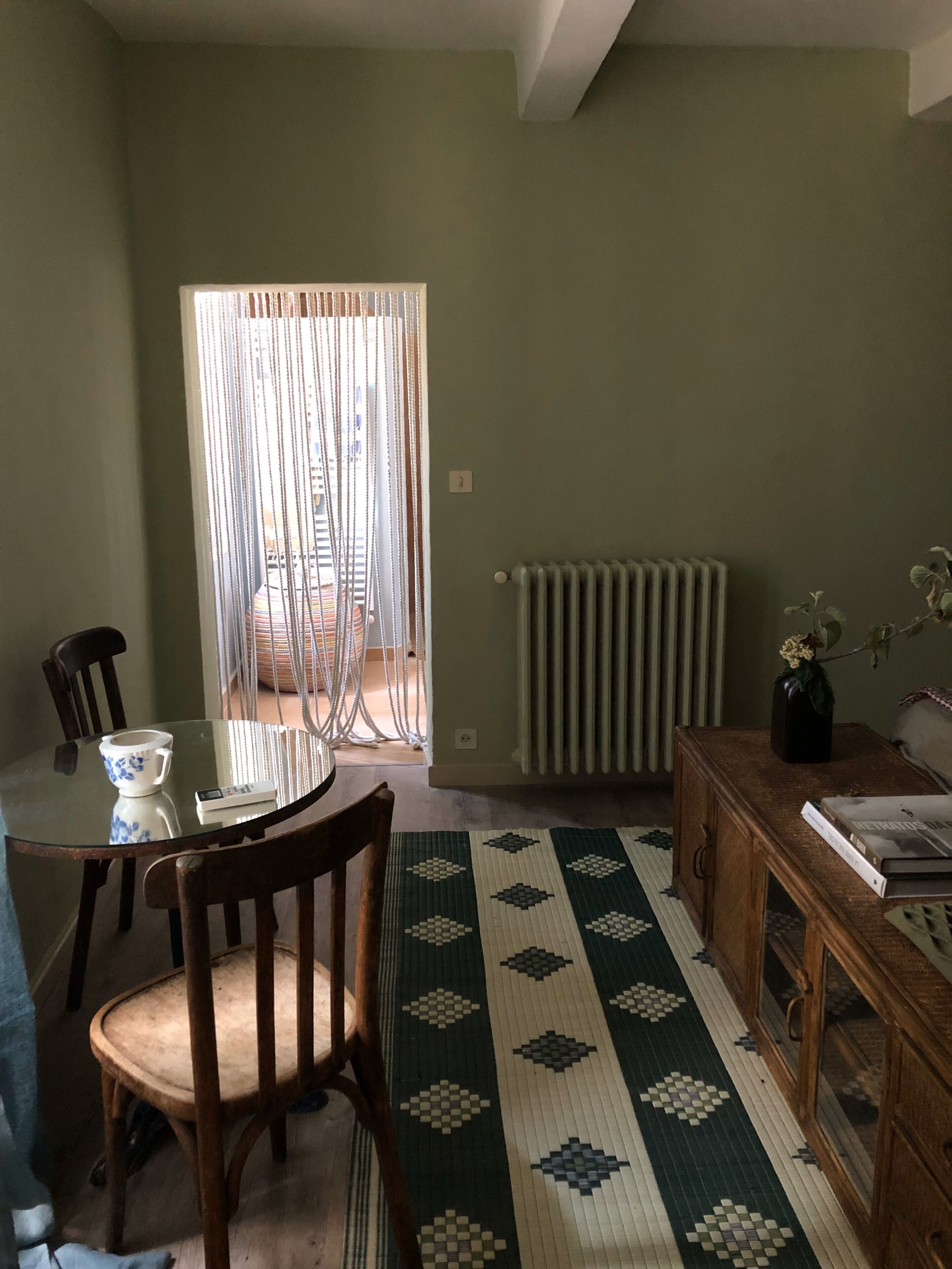 Un coin repas comprenant une table en verre, des chaises, un tapis à motifs, un radiateur et une bibliothèque.