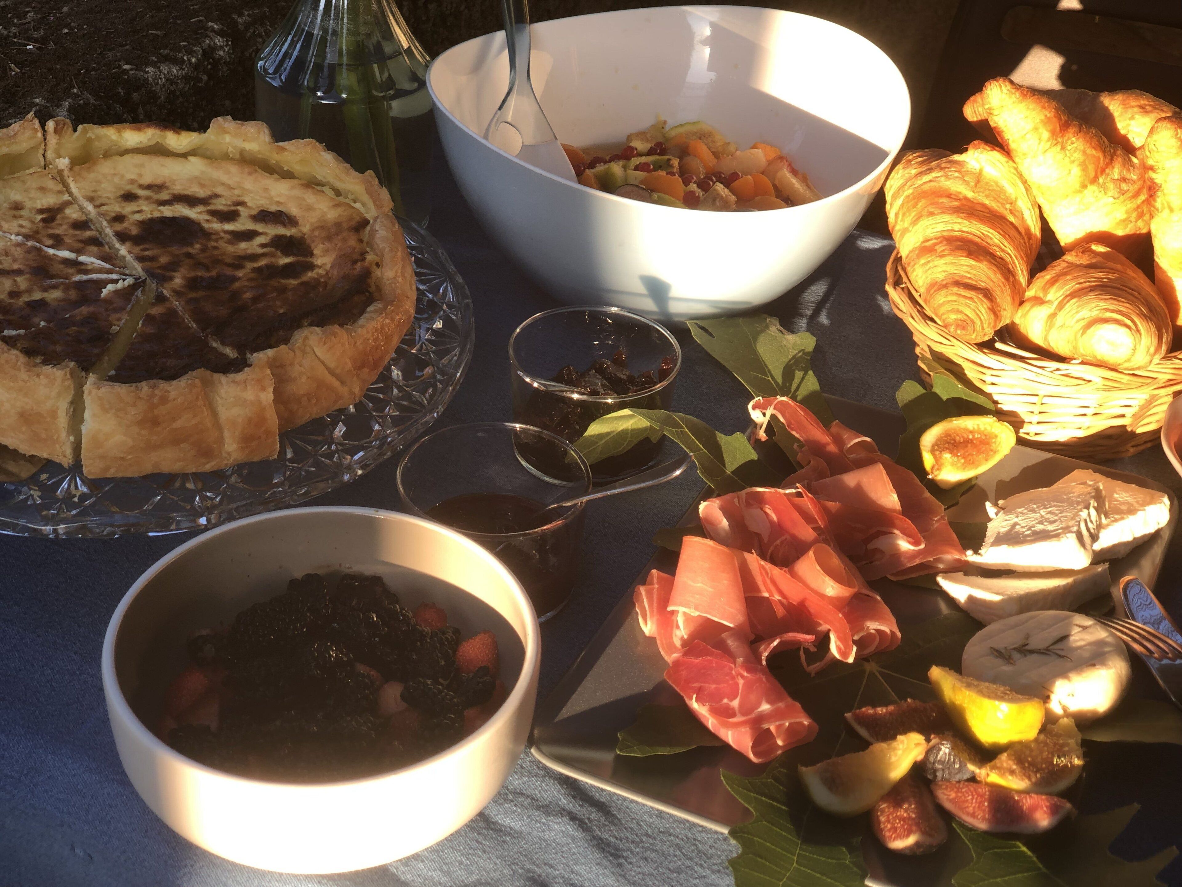 Une table sur laquelle on trouve divers aliments, notamment une tarte, un bol de soupe et une assiette garnie de viandes et de fruits.