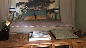Un dormitorio con una cama, dos lámparas de noche, una mesita de noche con libros y un cuenco decorativo, y un mural grande en la pared.