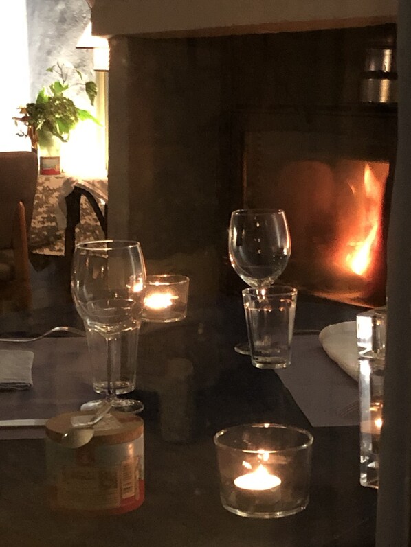 Una mesa con velas y copas, un tarro de velas y una planta al fondo.
