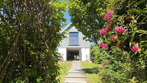 En stig som leder fram till ett hus omgivet av frodig grönska och rosa blommor.