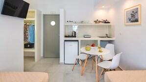 Habitación de hotel compacta con kitchenette, zona de comedor con mesa y sillas, cama y televisión montada en la pared.