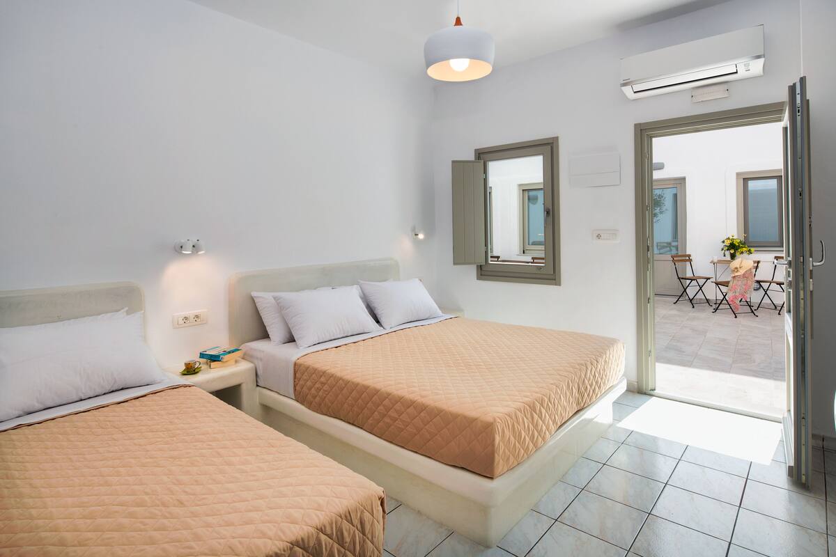 Habitación de hotel con dos camas, una mesita pequeña con una silla, un ventanal y un equipo de aire acondicionado.