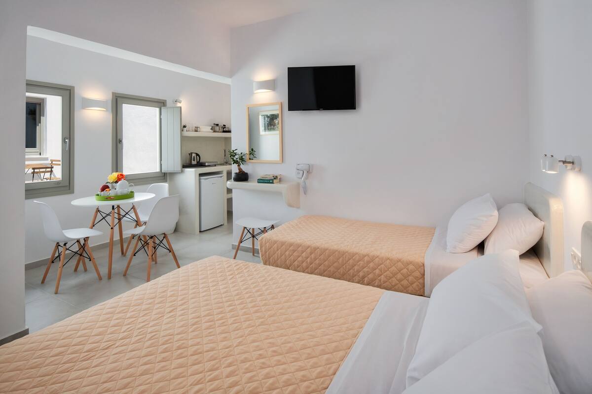 Habitación de hotel con dos camas, un escritorio con sillas, un televisor y una pequeña kitchenette.