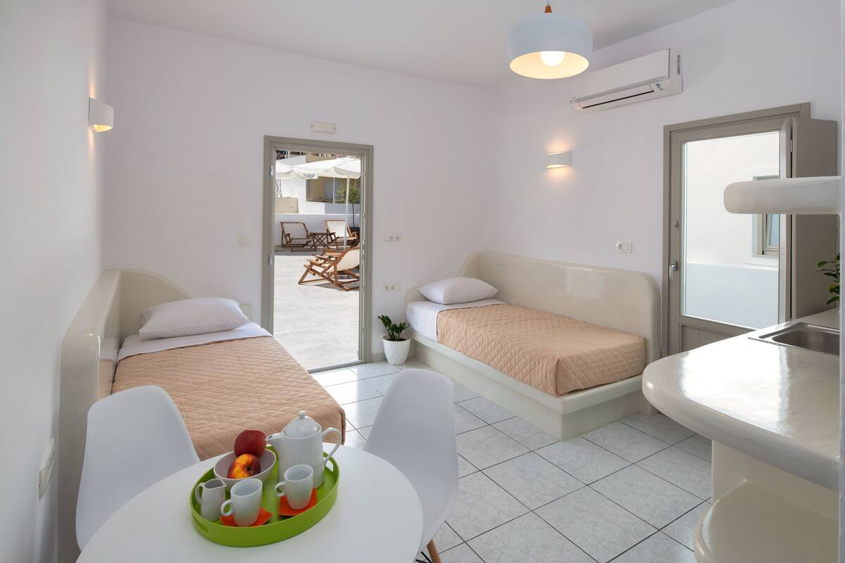 Una habitación de hotel moderna con dos camas, un rincón de comedor con mesa y sillas, y una kitchenette.