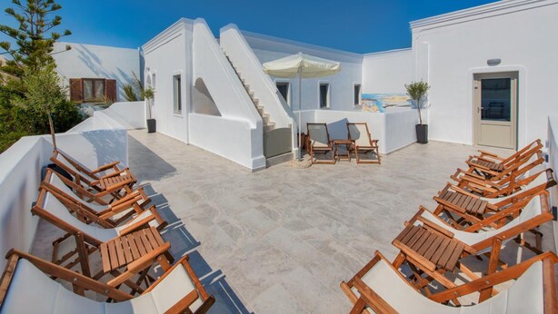 Un edificio blanco con una escalera, sillones de madera y un patio con baldosas.