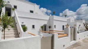 Un edificio blanco con una escalera que lleva a una terraza de madera, rodeado de muros blancos y ventanas pequeñas.