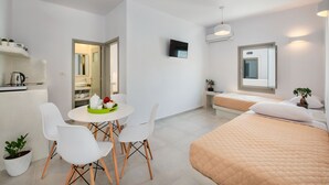 Una habitación de hotel moderna con cama, mesa de comedor con sillas, televisor y kitchenette.