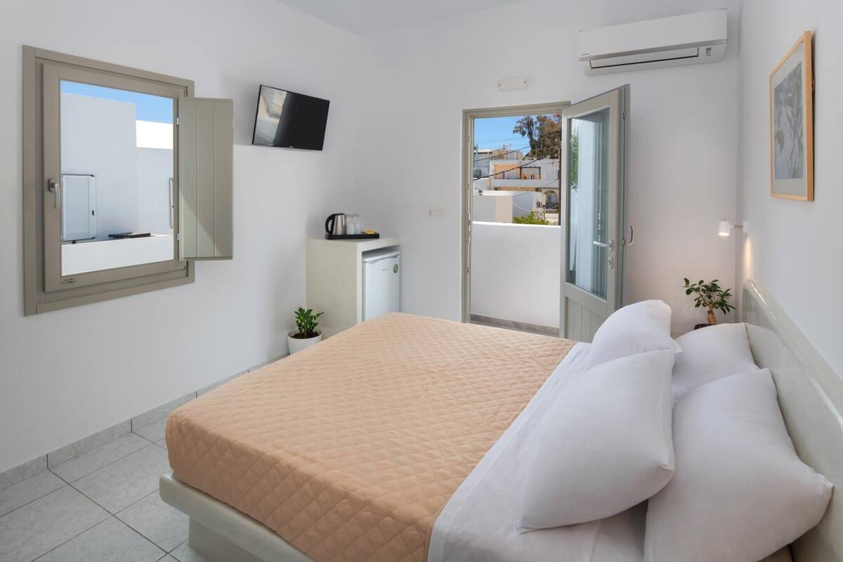 Un dormitorio con cama, televisor, kitchenette pequeña y balcón.