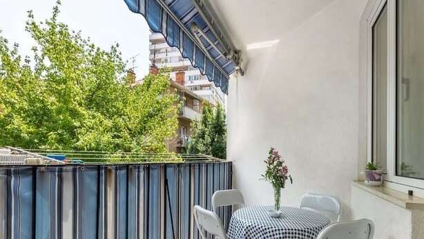 Un balcon agrémenté d’un auvent à rayures, de chaises blanches, d’une petite table et d’une plante en pot.