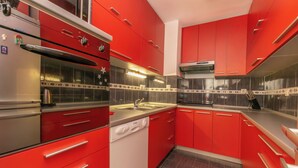 Une cuisine moderne avec des meubles de couleur rouge, des appareils en acier inoxydable et un dosseret carrelé.
