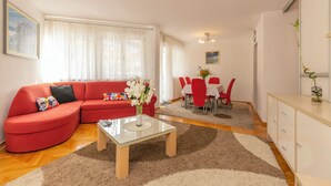 Un salon avec un canapé rouge, une table basse en verre et un coin repas avec des chaises rouges.