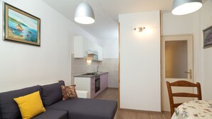 A compact living space with a sofa, a dining table, a kitchen area, and a door leading to another room. - Apartment Anica (Split)