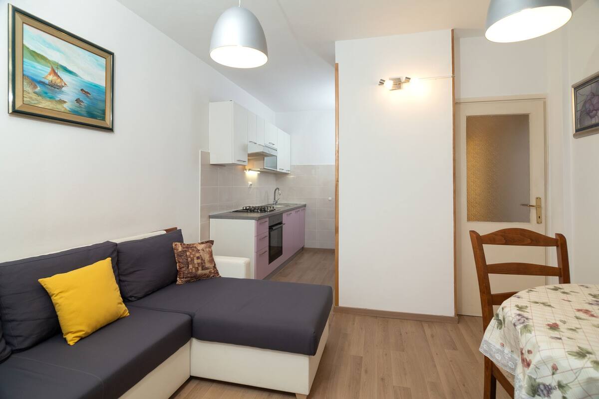 A compact living space with a sofa, a dining table, a kitchen area, and a door leading to another room.