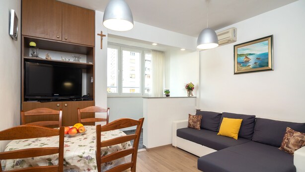 A compact living space with a dining table, chairs, a sofa, a TV, and a window with a view of buildings. - Apartment Anica (Split)