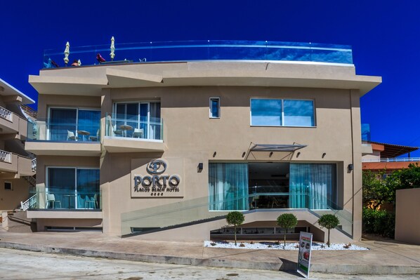 A modern hotel with a prominent sign, balconies, and a clear blue sky. - Porto Planos Beach Hotel (Zakynthos)