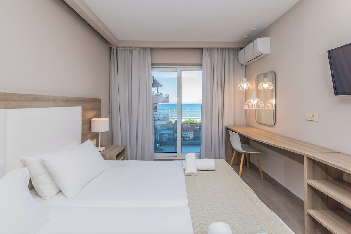 Una habitación de hotel con cama, escritorio, silla y un ventanal con cortinas.
