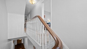 A staircase with a wooden handrail and white balusters, leading to a landing with a light fixture.