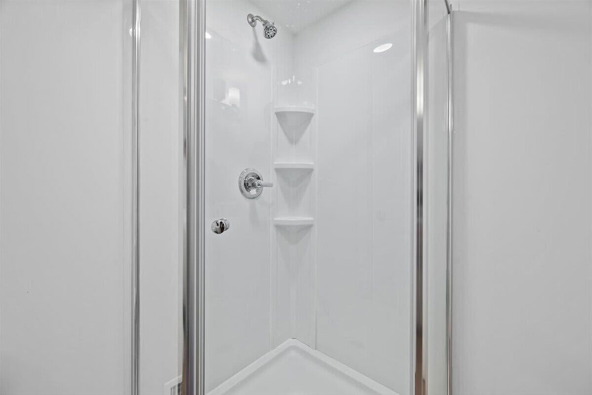Una cabina doccia in vetro con soffione e due ripiani.