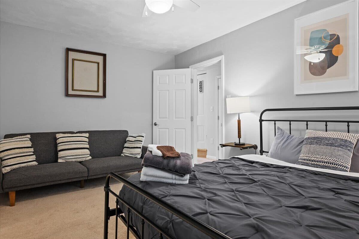 Een slaapkamer met een bed, een bank, een nachtkastje en een ingelijst kunstwerk aan de muur.