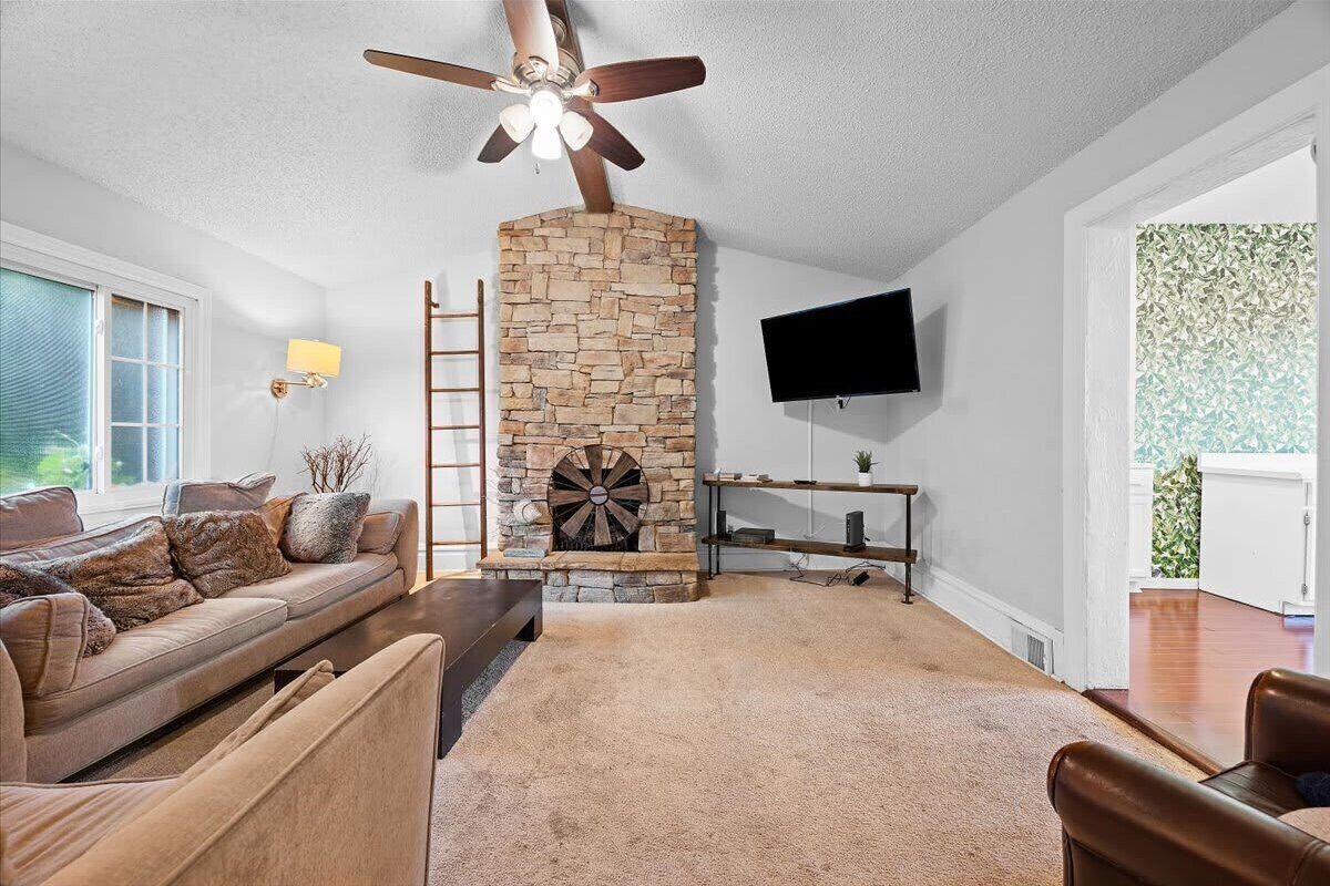 A living room with a stone fireplace, a ceiling fan, a TV mounted on the wall, and a sofa with cushions.