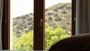A bedroom with a bed, wooden door, and a view of a hillside with greenery.