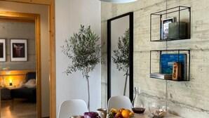 A dining area with a table set for two, featuring a modern pendant light, a vase with flowers, and a fruit bowl.