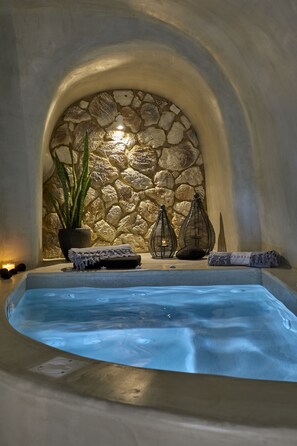 A spa area with a stone wall, a hot tub, and decorative items like candles and a plant. - Floria Suites (Santorini)