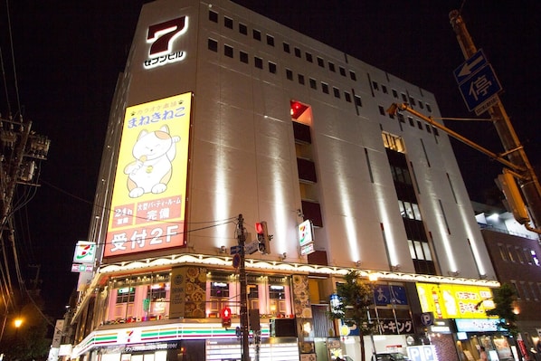 A multi-story building with a prominent 7-Eleven sign, a large advertisement featuring a cartoon cat, and various illuminated storefronts at the ground level.