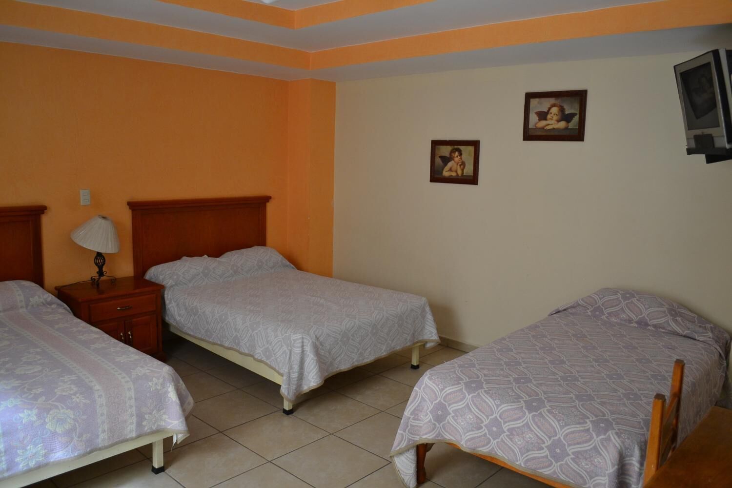 A room with two single beds, a nightstand with a lamp, and two framed pictures on the wall.