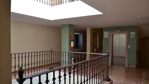 Eine Hotelhalle mit Treppe, Feuerlöscher, Aufzug und einem Schild, das den Standort des Aufzugs anzeigt.