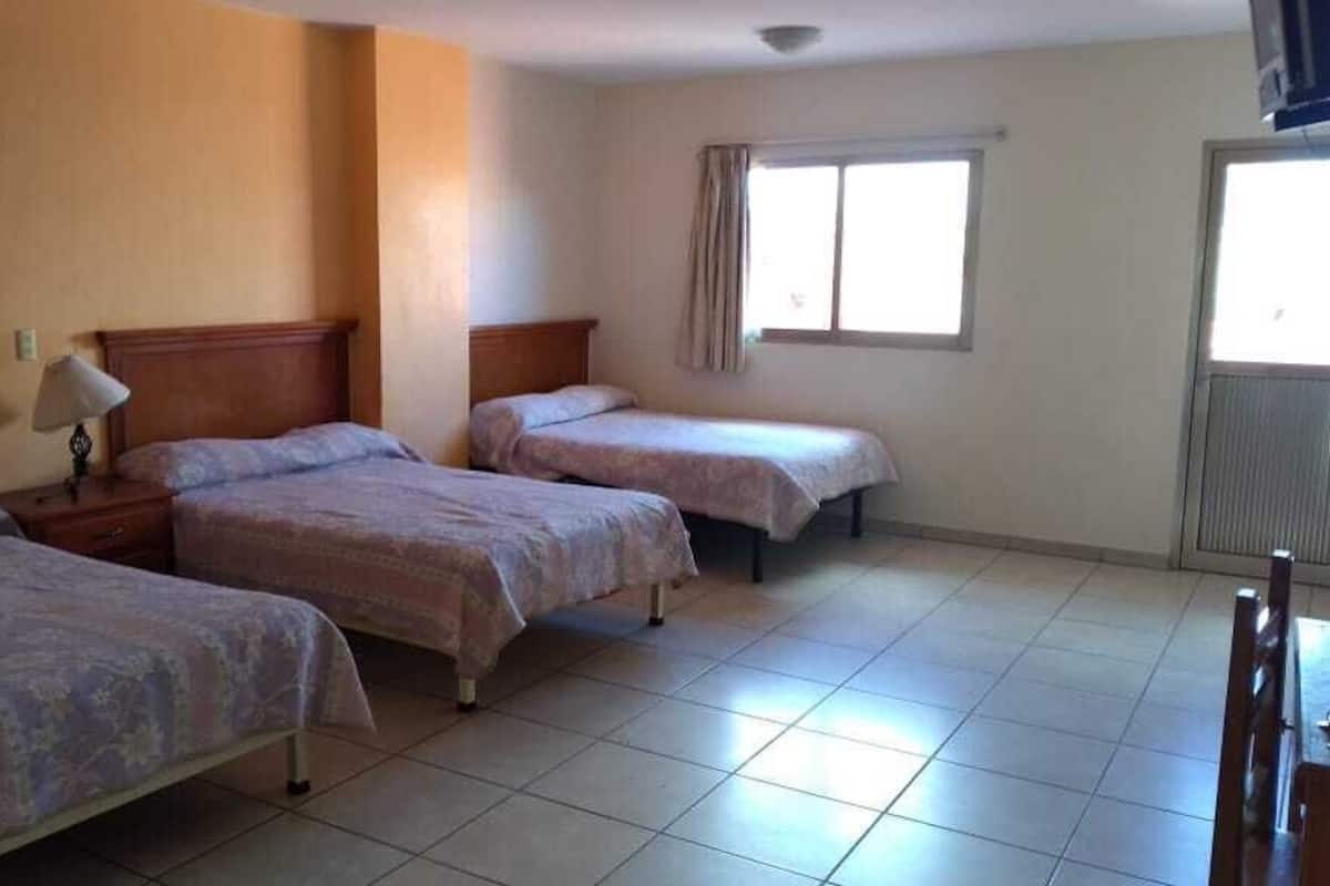 A hotel room with three beds, a window with curtains, and a radiator.