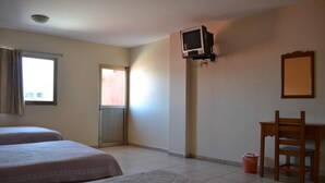 Ein Hotelzimmer mit zwei Betten, einem Schreibtisch, einem Sessel, einem an der Wand befestigten Fernseher und einem Fenster mit Vorhängen.