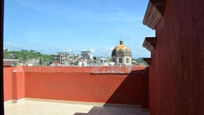 Eine Dachterrasse mit roter Wand und Fliesenboden, mit Blick auf eine Stadtlandschaft, dominiert von einem Gebäude mit goldener Kuppel.
