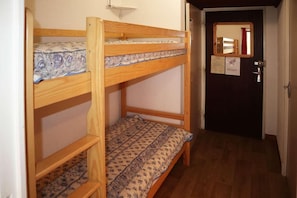 Ein Stockbett mit gemusterten Betttextilien, eine Tür mit Spiegel und ein Flur mit Holzboden.