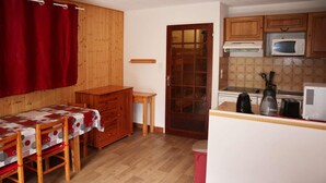 A compact kitchen with wooden cabinets, a microwave, a kettle, and a small table with a red tablecloth. - 1st floor, balcony, 32m², Les Orres (Les Orres)
