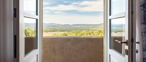 An open door with a view of a balcony overlooking a landscape with hills and trees.