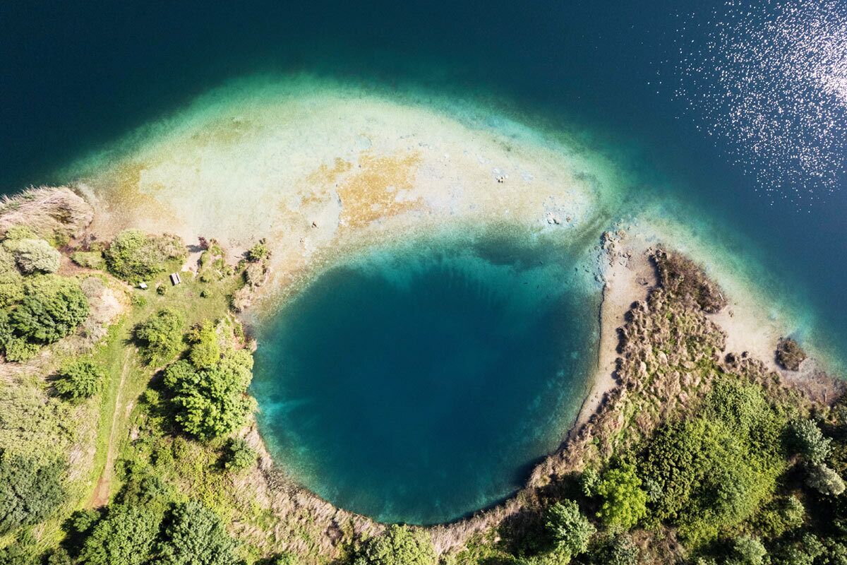 Una vista aerea di una zona costiera con una limpida laguna blu, circondata da fitta vegetazione verde e coste rocciose.