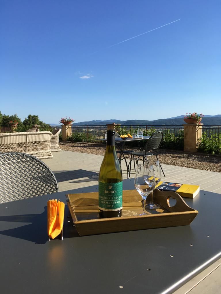 Ein Tisch mit einer Weinflasche, Gläsern und einer Schale auf einer Terrasse mit Blick auf Berge.