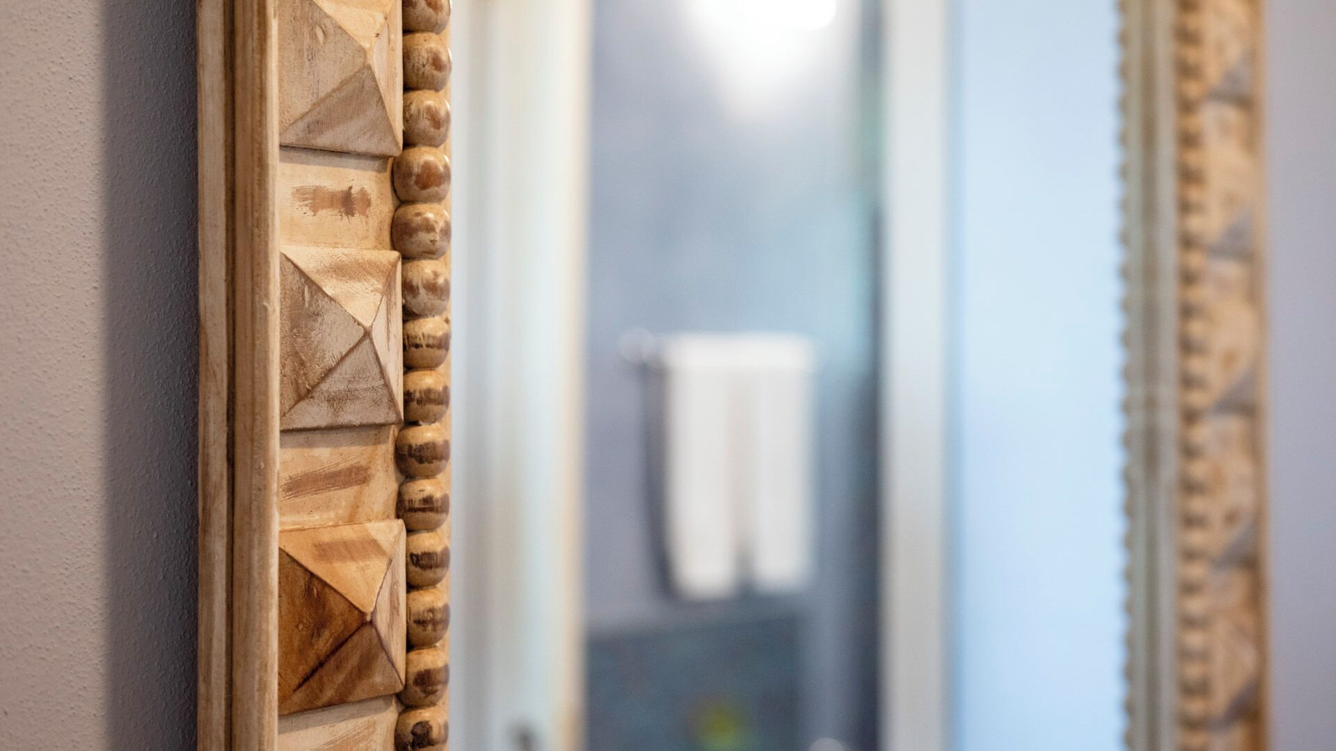 A wooden wall panel with geometric carvings and a mirror reflecting a bathroom with a towel rack.