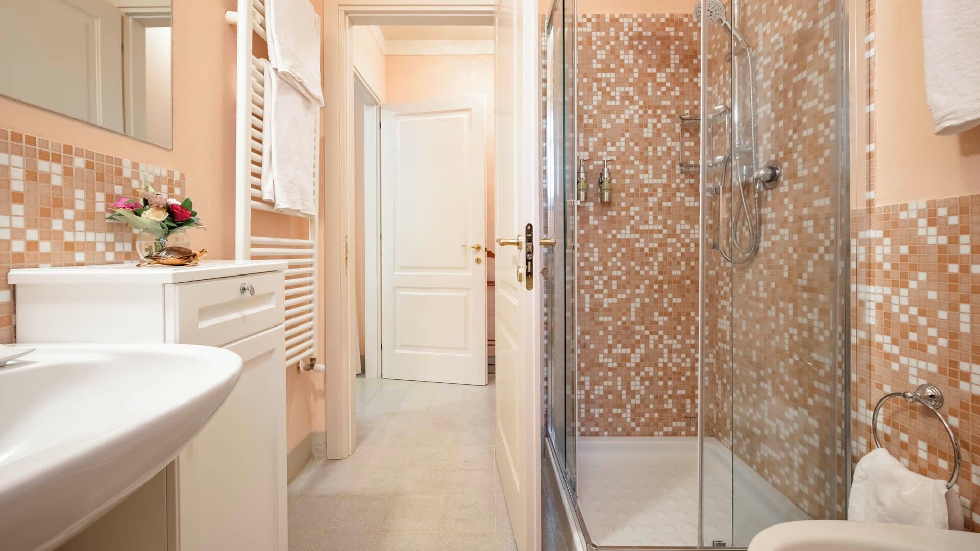 Un baño con ducha de vidrio, lavamanos blanco y salpicadero de azulejos.